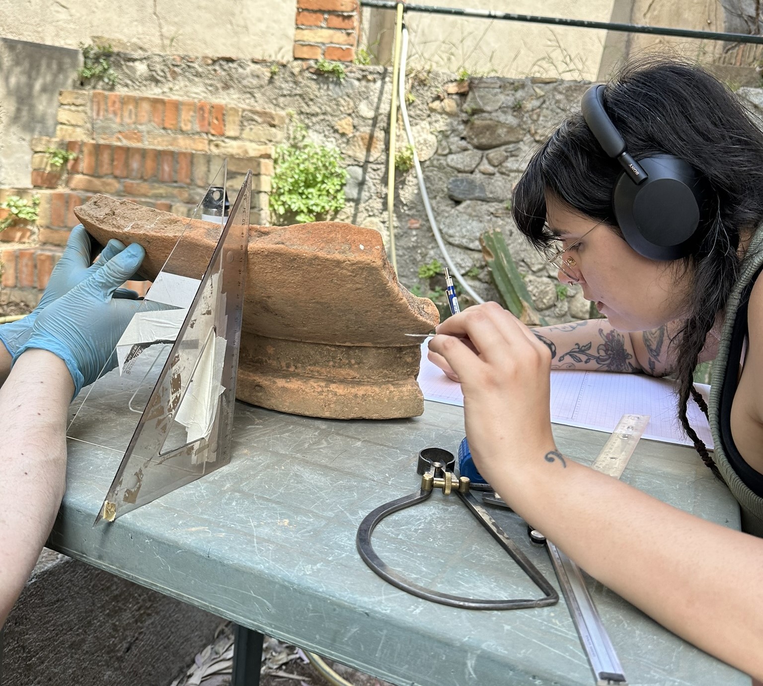 a woman wearing headphones works on drawing a large ceramic vessel