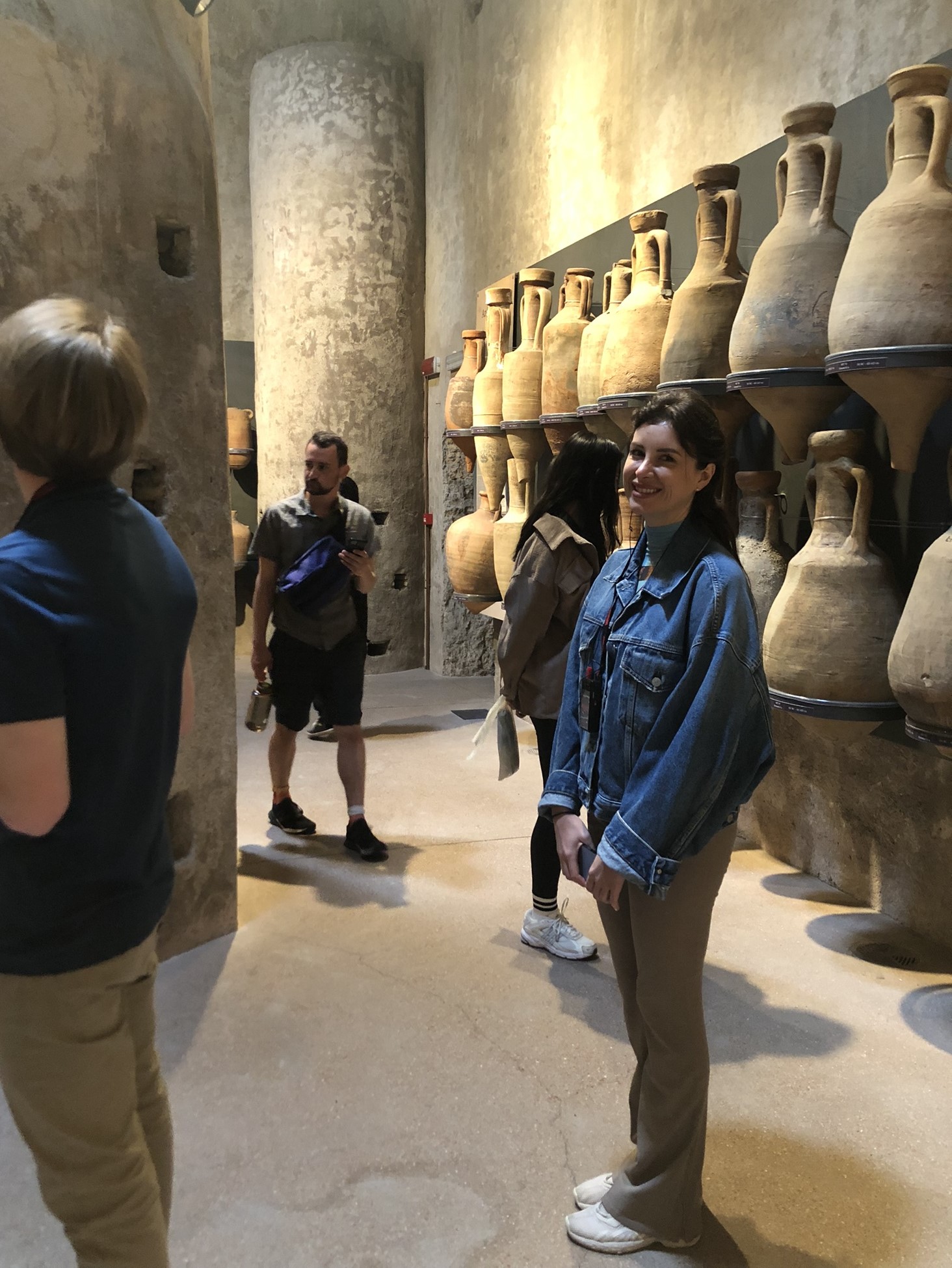 a woman stands in front of ancient amphoras