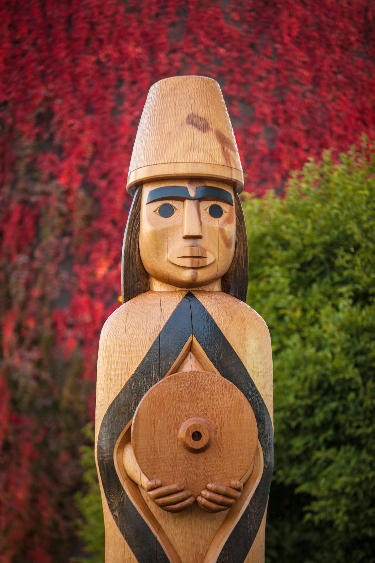 The Musqueam house post on campus wears a blanket and holds a spindle whorl